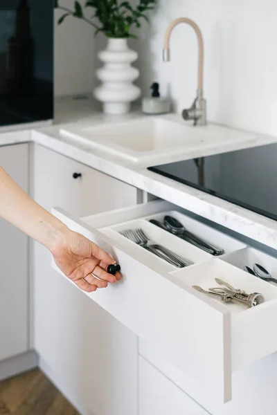 Cropped view of woman open white cutlery drawer in a modern apartment. Housewife holding clean shiny silverware in box with separate sections. Concept organization of space at kitchen