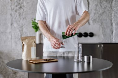 closeup of male hands put tea leaves from packaging in glass bottle for brewing herbal drink at kitchen room or alternative method of preparing chinese tea in infuser