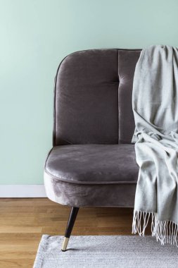 Close up view of soft bed throw over comfort grey couch in loft style living room. Modern armchair with plaid in bedroom. Sofa on carpet at wooden floor. Concepts oh hygge interior