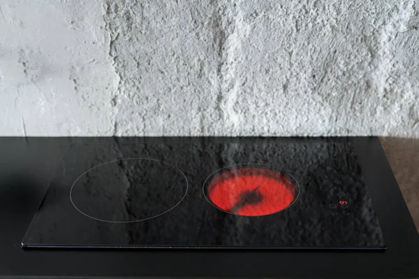 close up of electric stove with hot red burner and control panel with button. built in appliance against copy space wall at kitchen room in apartment with loft interior design