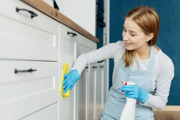 Portrait of smiling lady wearing apron and gloves wiping kitchen furniture with detergent.Woman removing dirt. Cleaning service worker job. Housekeeping concept
