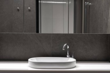 luxury hotel bathroom interior with modern washbasin on white countertop, silver water faucet, grey tile and mirror on wall indoors