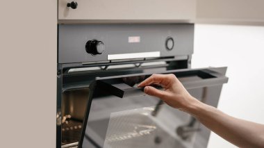 Woman opening glass door in electric oven with light inside. Housewife using empty microwave with a metal grid. Kitchen with built in household appliance, baking equipment