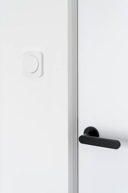 Cropped view of closed white door with black handle and light switches in modern apartment after renovation. Energy saving. Safety and comfort concept. Minimalistic house interior design