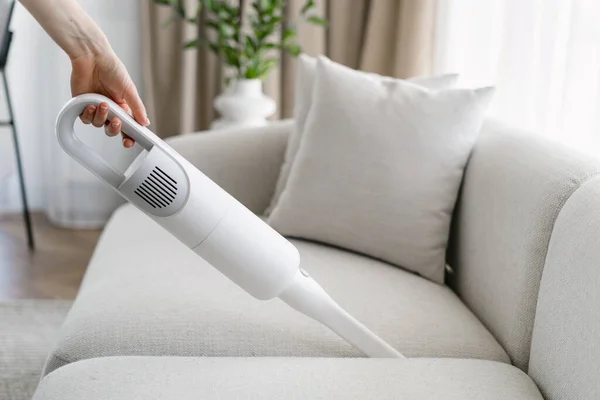 Side view of woman cleaning soft sofa using cordless vacuum in living room. Concept of cleanliness. Household equipment usage. Housewife chores. Cleaning service worker duties