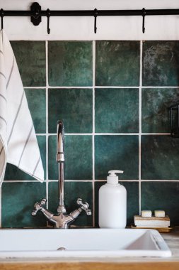 detail in kitchen interior, white sink, chrome water faucet, dispenser bottle with soap, washing eco sponge, dishwashing tablets, towel on wall with green tile