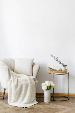 Elegant living room with classic design. Apartment interior with white textiled armchair in art deco style standing close to side table with home decor. Objects against white copy space wall
