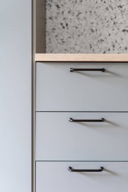 closeup of modern kitchen furniture or grey drawers with dark metal handles and wooden countertop in apartment