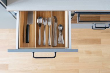keeping silverware in box from wood or opened drawer with spoons, forks, knife in modern kitchen cupboard