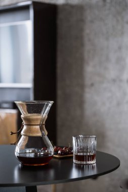 alternative method of brewing fresh coffee at home. glass chemex with hot brown caffeine beverage and wooden tray with sweet cherry on kitchen table