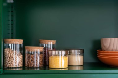 kitchenware, glass jars with beans, pasta and grains on metal green shelf at cabinet. storage food concept and order at kitchen