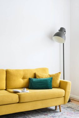 contemporary interior design in living room with velvet yellow couch and green pillow, black lamp and carpet on floor in apartment