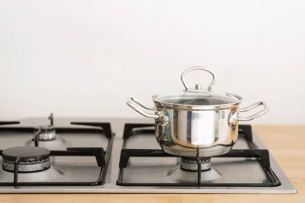stainless steel cooking pot with handles and glass lid on gas cooker built in wooden countertop at contemporary kitchen