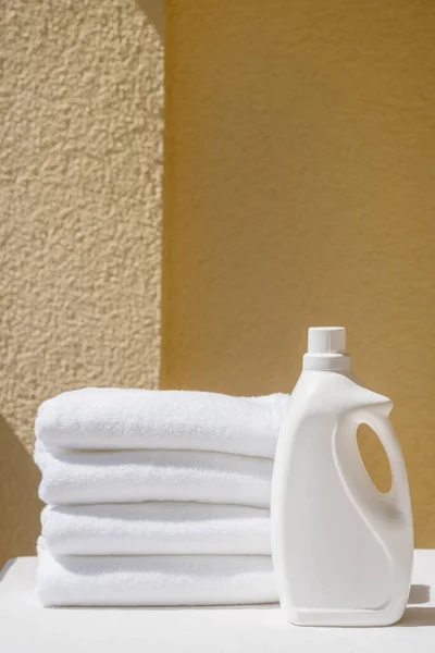 liquid cleaner gel for laundry in plastic mockup bottle, close to stack with clean fresh terry towels on yellow wall background