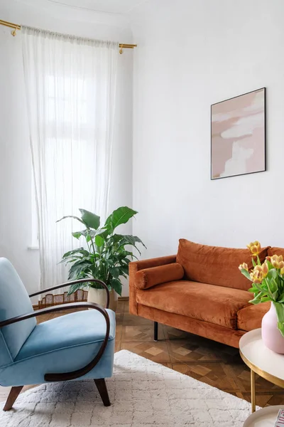 Part of retro living room interior with vintage furniture design in the style of the 80s. Bright apartment with orange couch, light blue armchair and potted plants. Spending weekend at home concept