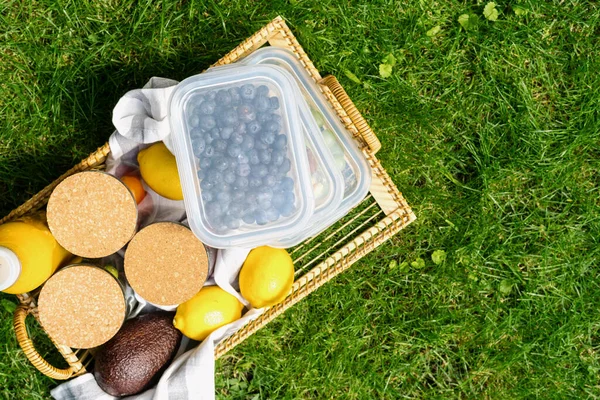 ガラス容器とリサイクルボックス食品用籐竹トレイ上のレモン アボカドと新鮮なジュースボトルで芝生の屋外 トップビュー — ストック写真