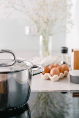 Modern ışık mutfağında cam seramik fırının kapağı olan tencereye, tezgahın üstünde yumurtalara ve bulanık arka plana odaklan.