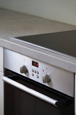 Mutfaktaki modern aletler, tezgahta elektrikli ocak ve düğmeli elektrikli fırın, regülatör düğmeleri ve kontrol panelinde zamanlayıcı.