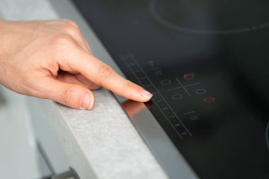 Elektrikli fırın hob 'un kontrol panelindeki kadın el düğmesine, ocağın siyah yüzeyindeki kırmızı göstergeye, modern ev aletlerine...