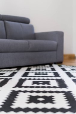 Geometrik desenli halı, gri rahat kanepenin yanında modern dairedeki İskandinav tarzı bulanık arka planı olan dinlenme odasında.
