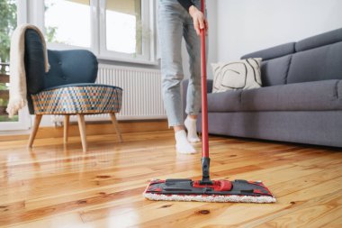 Kadınlar ellerindeki kırmızı plastik paspası tutarlar ve modern dairedeki odalarda parke yıkarlar. Kesilmiş atış, ev işi konsepti.