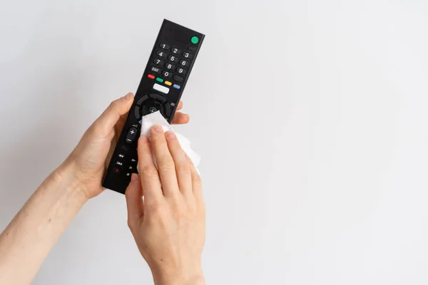 female hands hold tv remote control and wipe buttons with antiseptic cloth on white background with copy space, cropped shot, housework concept