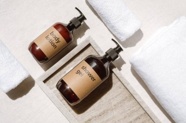 Duş jeli ve vücut losyonunun üstünde kahverengi plastik şişelerde şeker tepsisi, mermer tepsi ve beyaz terli havlular ev banyosunda, kişisel bakım konsepti.