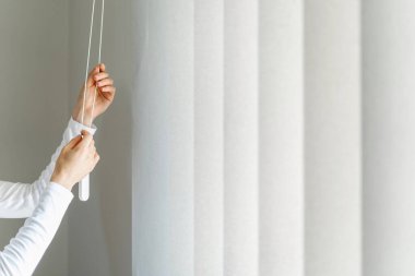 Kesilmiş kadın elleri ipi çeker ve oturma odasındaki pencerenin dikey camlarını açar. Modern evdeki kadın panjur ayarlama mekanizması