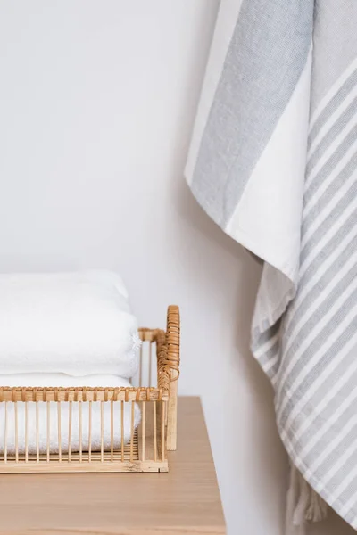 vertical shot of detail in bathroom interior, fresh towels folded in wicker tray on wooden shelf and beach towel hanging on wall, storage concept