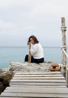 Uçurumun kenarında oturan kadın. Kameraya bakmak için döndü. Gözlüklü güzel bir kızın ön görüntüsü. Güvensiz ahşap bir köprüden geçiyorum.