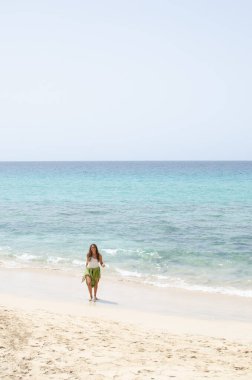 Sahilde yürüyen orta yaşlı güzel bir kadın. Mutlu, güçlü ve özgür hissediyor. giyinmiş kadın turist kanarya adalarında sahilde tek başına duruyor..