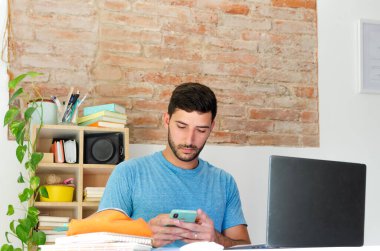 handsome student updates his social networks and searching for information on his computer. does his homework at home. young entrepreneur seeks new goals for his small business. back to school concept