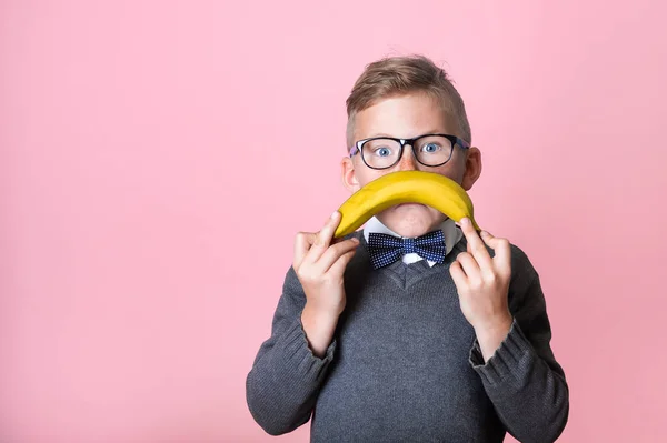 Portrait of school boy with sad sign isolated on pink background. Kid with sad emoticon face sign with banana. Child show bad mood — Stock Photo, Image
