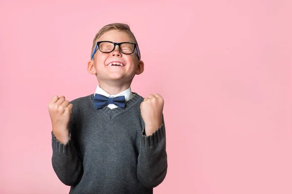 Happy kid with arms up celebrating winning isolated on pink background. Emotional portrait of child with raising hands. Confident school boy in glasses celebrating a triumph. Winner — Stock Photo, Image