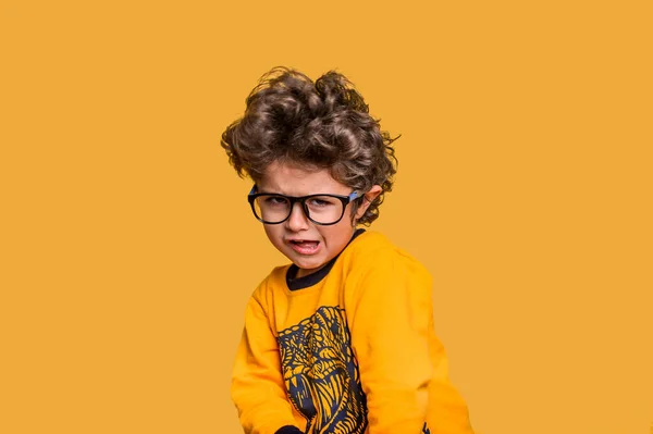 Portrait of five years old child making funny face. Boy in glasses tousled hair looking at camera with silly smile. Kid in yellow shirt isolated on yellow background. Hispanic cute child — Stock Photo, Image