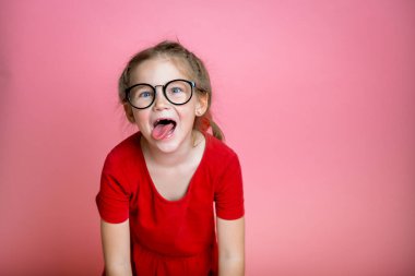 Kırmızı tişörtlü, gözleri biçen, kameraya gülümseyen ve dil gösteren, komik suratlar yapan aptal çocuk portresi. Çılgın suratlı okul çocuğu suratı. Mutlu inek çocuk. Okula geri dön.