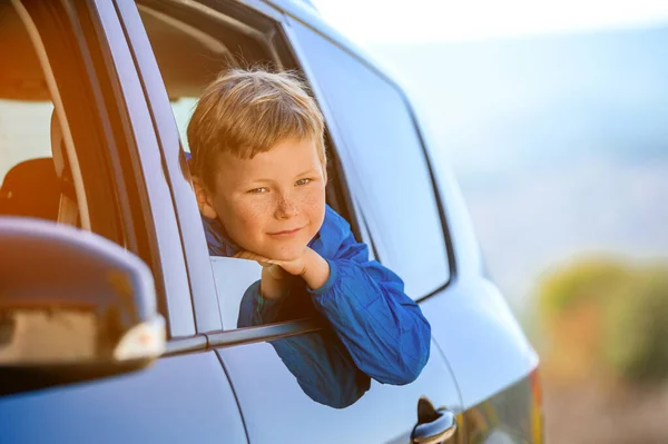 El chico feliz mira por la ventana del auto. Un niño feliz viajando en coche. Niño niño turista buscando en la hermosa naturaleza. Viajes familiares en coche por las montañas. Vacaciones de verano —  Fotos de Stock