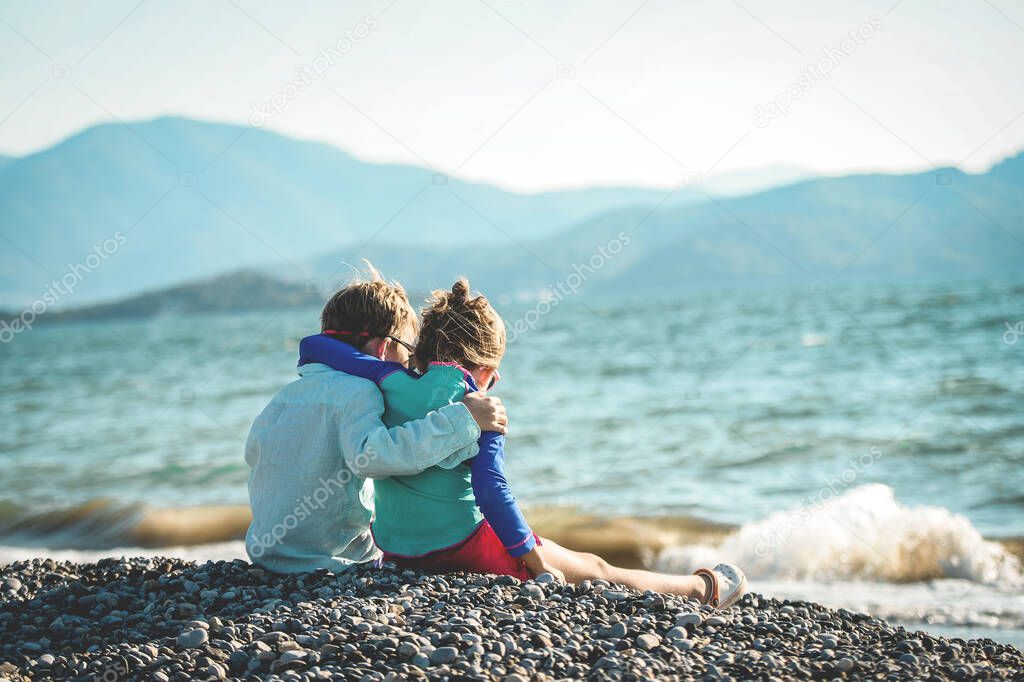 Couple kids hug each other on sea beach. Children playing with sand on summer beach. Happy children run at sea beach. Kids are playing merrily. Boy and girl look on beautiful nature