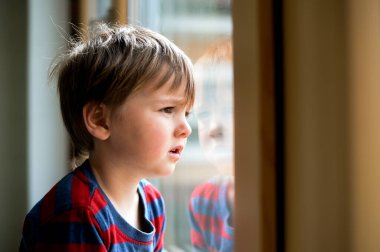 Pencereden bakan iki yaşında bir çocuk. Çocuk pencereden dışarı bakıyor. Pencere kenarında oturan bir çocuğun portresi