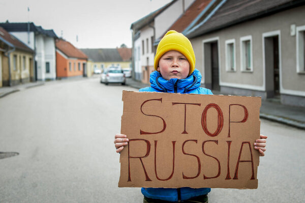 School boy with political banner Stop russia. Say no to putin the street protest rally. Kid in Ukrainian flag clothes with banner. Little ukrainian patriot boy support Ukraine. No war with Ukraine.