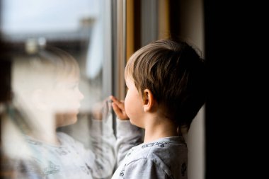 Küçük Ukraynalı çocuk pencereden bakıyor. Çocuk ayakta ve parmağıyla işaret ediyor. Yalnız çocuklar ve savaş. Rusya 'nın Ukrayna' ya saldırısı.