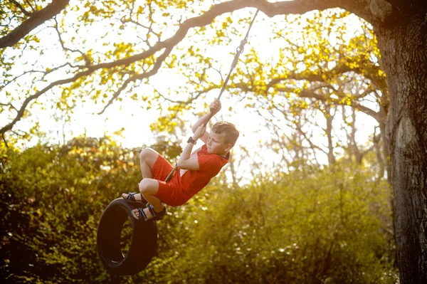 Niño feliz jugando swing neumático colgando en el patio de recreo. Los niños juegan en la escuela o jardín de infantes. Oscilación activa para niños Actividad saludable de verano para niños. Pequeño niño balanceándose en anillo de goma — Foto de Stock
