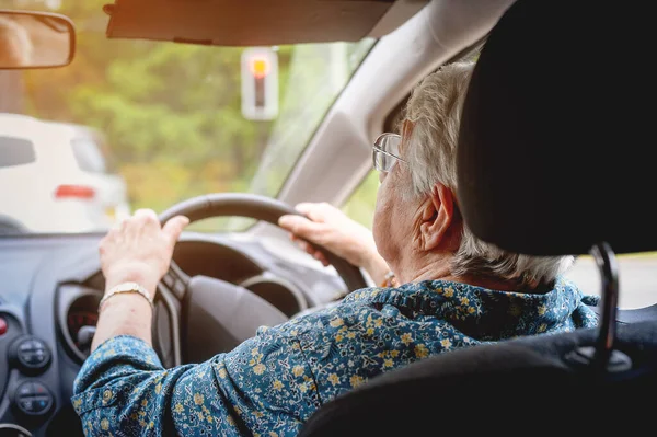 Cheerful senior woman driving a car. Old lady in glasses drive the car in glasses. Back view