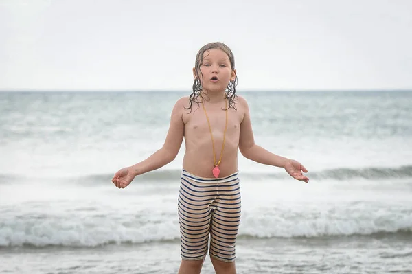 What. Why. Kid is asking. Emotions and a smile. Funny kid girl with surprised face and open hands with wet hair near sea. Funny surprised portrait of child. Sea beach. Vacation.
