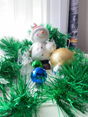 Beyaz bir masada kardan adam figürü, arka planda bir kitap. Noel süsleri. Yeni Yıl