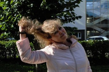 Uzun ve sağlıklı dalgalı saçları olan gülümseyen bir kadının portresi. Güzel genç bayan parka bakıyor. Sonbahar aydınlık, güneş yüzünde parlıyor. Saç bakımı