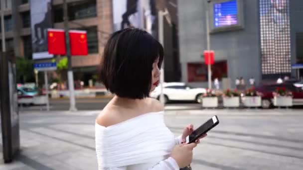 漂亮的亚洲模特拿着智能手机走路 在中国 一个时髦的中国女孩拿着手机走在大街上 现代女性购物 — 图库视频影像