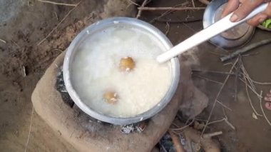 Hintli bir kadın ahşap bir fırında pirinç pişiriyor. Hint köyünde geleneksel yemek pişirme tarzı. Pirincin yanı sıra patatesler de kaynıyor. odun ateşi.
