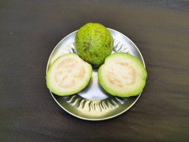  Slice guava on plate in black background. Its other names common guava, Psidium guajava, lemon guava, apple guava. This is is a small tree in the myrtlefamily. 