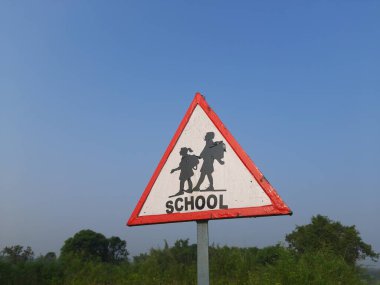 Yol kenarında okul tabelası var. Yol kenarındaki üç köşeli okul levhası. Yavaş sür işareti. Hindistan 'da okul geçidi işareti.
